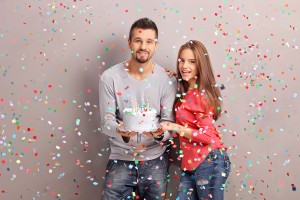 Young joyful couple holding a birthday cake with a lot of confet